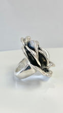 Load image into Gallery viewer, A sterling silver ring featuring a sculpted flower design with textured petals, photographed on a clean white surface against a light gray background.
