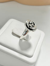 Load image into Gallery viewer, A polished silver ring featuring an openwork rose design with a black inlay, displayed on a white jewelry stand.
