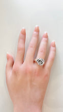 Load image into Gallery viewer, A hand with a French manicure wearing a silver ring shaped like a rose, resting on a plain off-white surface.
