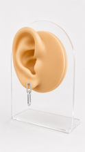 Load image into Gallery viewer, A beige silicone ear model attached to a clear acrylic stand, with a small silver 925 paperclip hanging from the earlobe, photographed on a white background.
