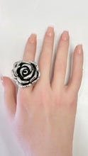 Load image into Gallery viewer, A hand with manicured nails wearing a large, textured silver ring shaped like a rose, shown against a plain white background.
